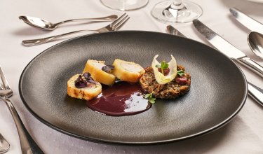 Schwarzer Teller mit drei panierten Fleischstücken, dunkler Sauce und Pilzgericht mit Garnitur