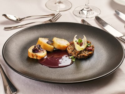 Schwarzer Teller mit drei panierten Fleischstücken, dunkler Sauce und Pilzgericht mit Garnitur