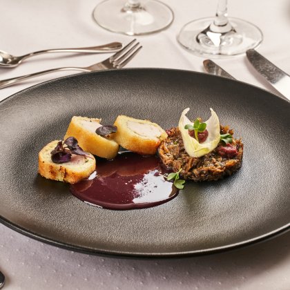 Schwarzer Teller mit drei panierten Fleischstücken, dunkler Sauce und Pilzgericht mit Garnitur