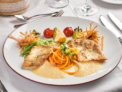 Gebratene Fischfilets mit Gemüse, Zitronenschnitz und Sauce auf weißem Teller angerichtet