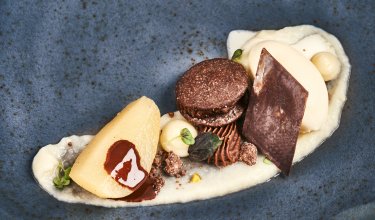 Fein angerichtetes Dessert mit Birne, Schokoladencreme, Schokoladenstück und Vanilleeis auf blauem Teller