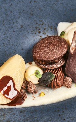 Fein angerichtetes Dessert mit Birne, Schokoladencreme, Schokoladenstück und Vanilleeis auf blauem Teller