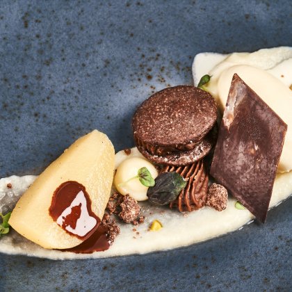 Fein angerichtetes Dessert mit Birne, Schokoladencreme, Schokoladenstück und Vanilleeis auf blauem Teller
