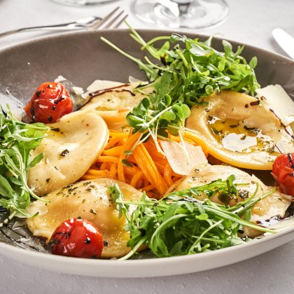 Teller mit Ravioli, Rucola, gerösteten Kirschtomaten und Karottenstreifen auf weißem Tisch