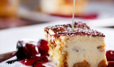 Nahaufnahme eines Stücks Tiramisu mit Lavendelblüte auf weißem Teller mit Kirschsoße