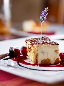 Nahaufnahme eines Stücks Tiramisu mit Lavendelblüte auf weißem Teller mit Kirschsoße