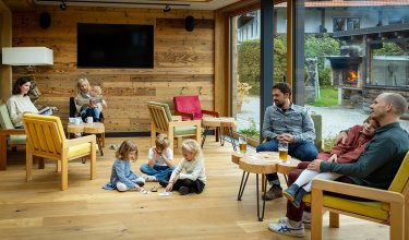 Gemütlicher Raum mit Holzwänden, Erwachsenen auf Sesseln und Kindern, die auf dem Boden spielen