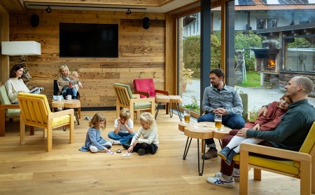 Gemütlicher Raum mit Holzwänden, Erwachsenen auf Sesseln und Kindern, die auf dem Boden spielen