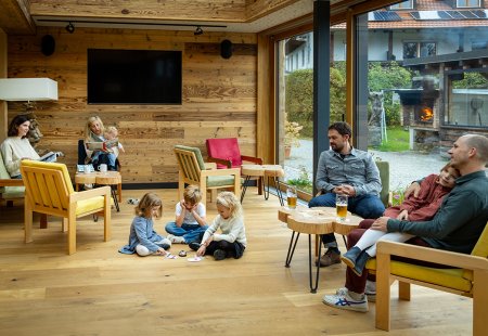 Gemütlicher Raum mit Holzwänden, Erwachsenen auf Sesseln und Kindern, die auf dem Boden spielen