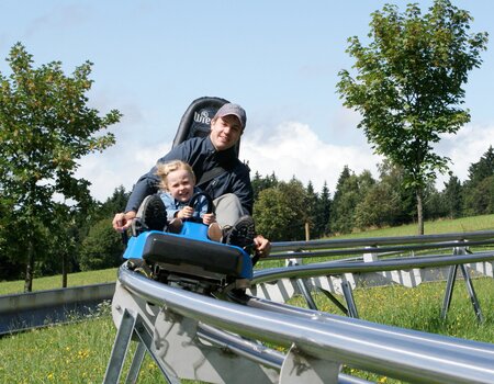 Vater mit Tochter auf der Sommerrodelbahn