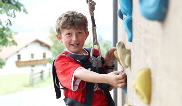 Junge klettert an einer Kletterwand mit bunten Griffen und trägt Kletterausrüstung
