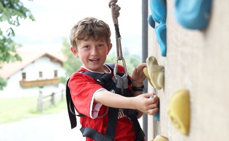 Junge klettert an einer Kletterwand mit bunten Griffen und trägt Kletterausrüstung