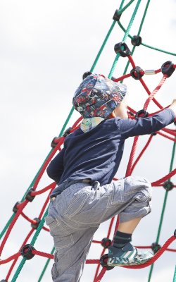 Kind klettert an einem roten und grünen Kletternetz auf einem Spielplatz