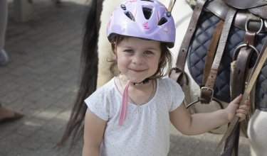 Kind mit lila Helm hält Pferdegeschirr und steht neben einem gesattelten Pferd