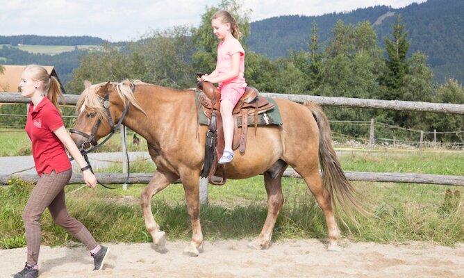 Reitlehrerin führt Mädchen auf Pferd