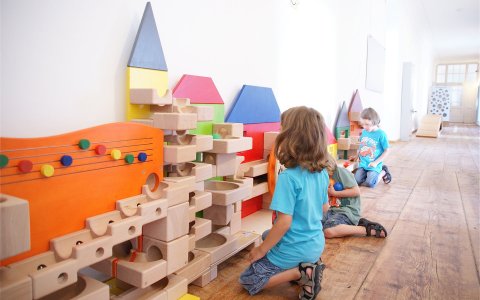 Kinder spielen auf dem Boden mit bunten Holzbausteinen und Kugelbahnen an der Wand