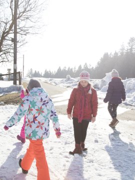 Kinder in bunter Winterkleidung spielen auf verschneitem Weg mit Wald im Hintergrund