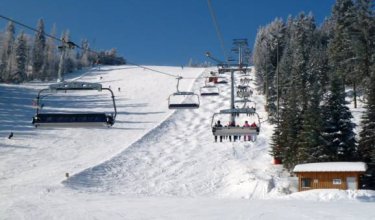 Skilift mit Sesseln fährt über schneebedeckten Hang neben verschneiten Bäumen unter blauem Himmel