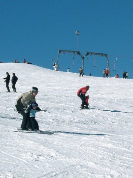 Verschiedene Menschen beim Skifahren auf schneebedecktem Hang unter klarem blauem Himmel mit Skilift im Hintergrund