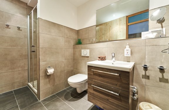 Modernes Badezimmer mit Dusche links, Toilette in der Mitte und Waschbecken mit Spiegel rechts