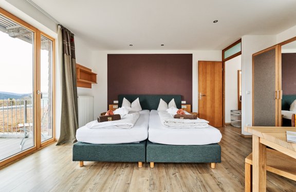 Modernes Schlafzimmer mit zwei Einzelbetten, Holzboden, Balkon links und Holzmöbeln rechts