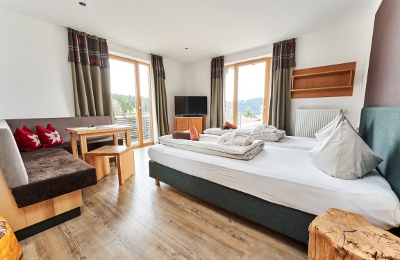 Helles Hotelzimmer mit Doppelbett, Sitzecke, TV und großen Fenstern mit Blick auf die Berge