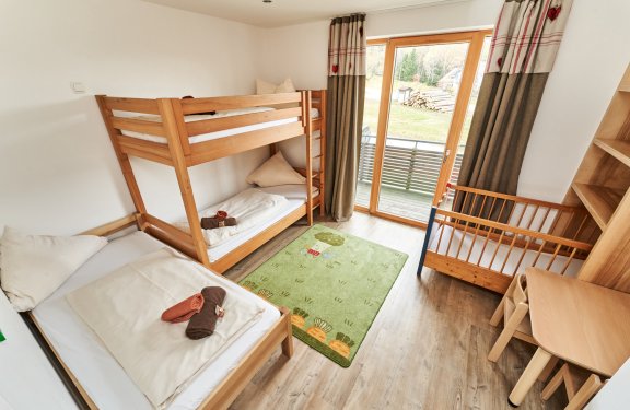 Kinderzimmer mit Etagenbett, Einzelbett, Babybett, grünem Teppich und Balkon mit Vorhängen