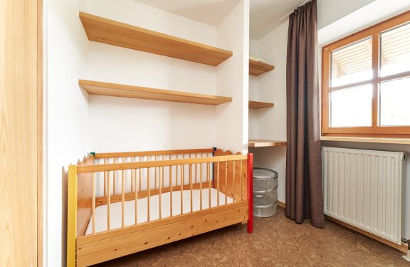 Kinderbett aus Holz in der Ecke eines Zimmers mit Regalen und Fenster mit Vorhang
