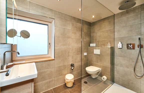 Modernes Badezimmer mit Waschbecken links, Toilette in der Mitte und Dusche rechts mit Glaswand