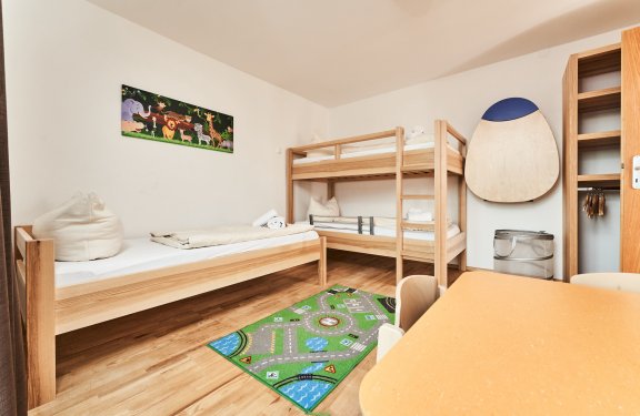 Kinderzimmer mit Etagenbett, Einzelbett, buntem Spielteppich und Tierbild an der Wand