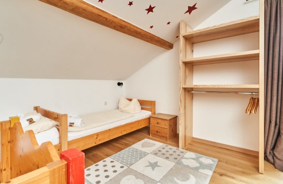 Kinderzimmer mit Holzbett, Nachttisch, offenem Kleiderschrank und Teppich mit Sternen und Herzen