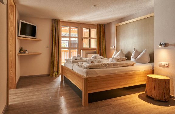 Hell eingerichtetes Schlafzimmer mit Doppelbett, Holzstamm als Nachttisch und Fernseher an der Wand