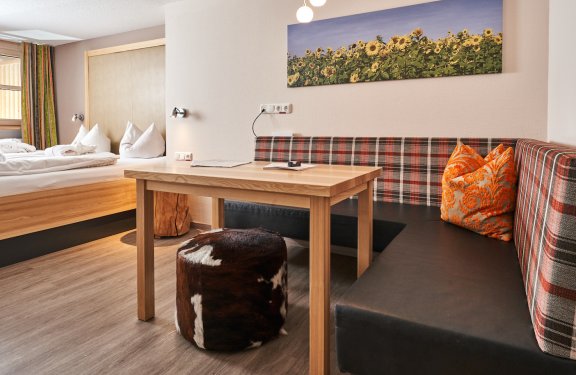 Gemütliche Sitzecke mit Holz­tisch, kariertem Sofa und Sonnenblumenbild an der Wand