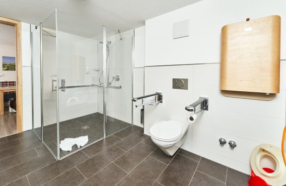 Barrierefreies Badezimmer mit ebenerdiger Dusche, Wandtoilette und Wickeltisch an der Wand