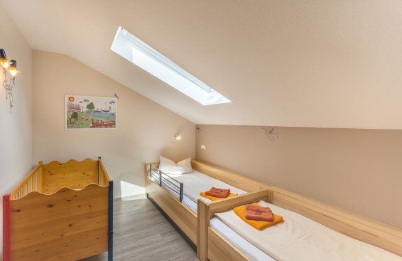 Schräges Kinderzimmer mit zwei Einzelbetten und einem Holz-Kinderbett unter einem Dachfenster