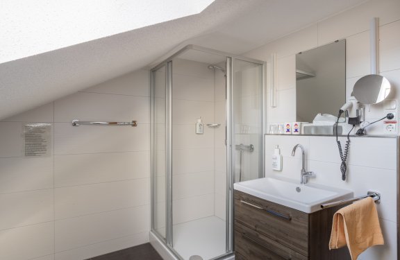 Badezimmer mit Duschkabine unter schräger Decke, Waschbecken mit Spiegel und Haartrockner