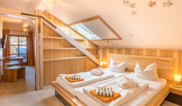 Gemütliches Schlafzimmer mit Dachfenster, Holzmöbeln und Blick in einen angrenzenden Raum mit Tisch
