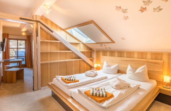 Gemütliches Schlafzimmer mit Dachfenster, Holzmöbeln und Blick in einen angrenzenden Raum mit Tisch