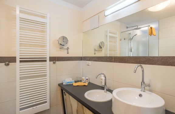 Helles Badezimmer mit zwei Waschbecken, großem Spiegel und Handtuchheizung an der Wand