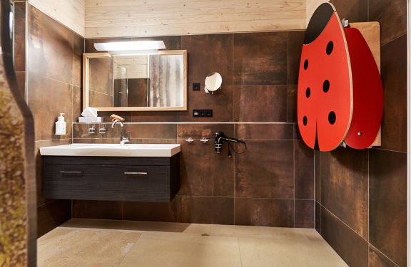 Modernes Badezimmer mit Waschbecken, Spiegel und einem roten Marienkäfer-Wickeltisch an der Wand