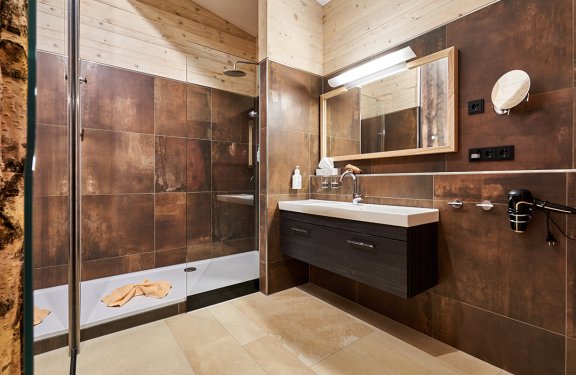 Modernes Badezimmer mit braunen Fliesen, großer Dusche links und Waschbecken mit Spiegel rechts