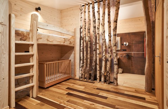 Holzraum mit Etagenbett, Kinderbett und Raumteiler aus Baumstämmen neben offenem Badbereich