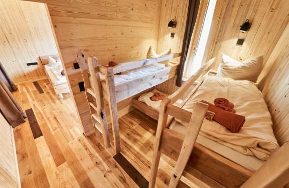 Holzraum mit Etagenbett und Einzelbett, weiße Bettwäsche und orange Handtücher auf den Betten